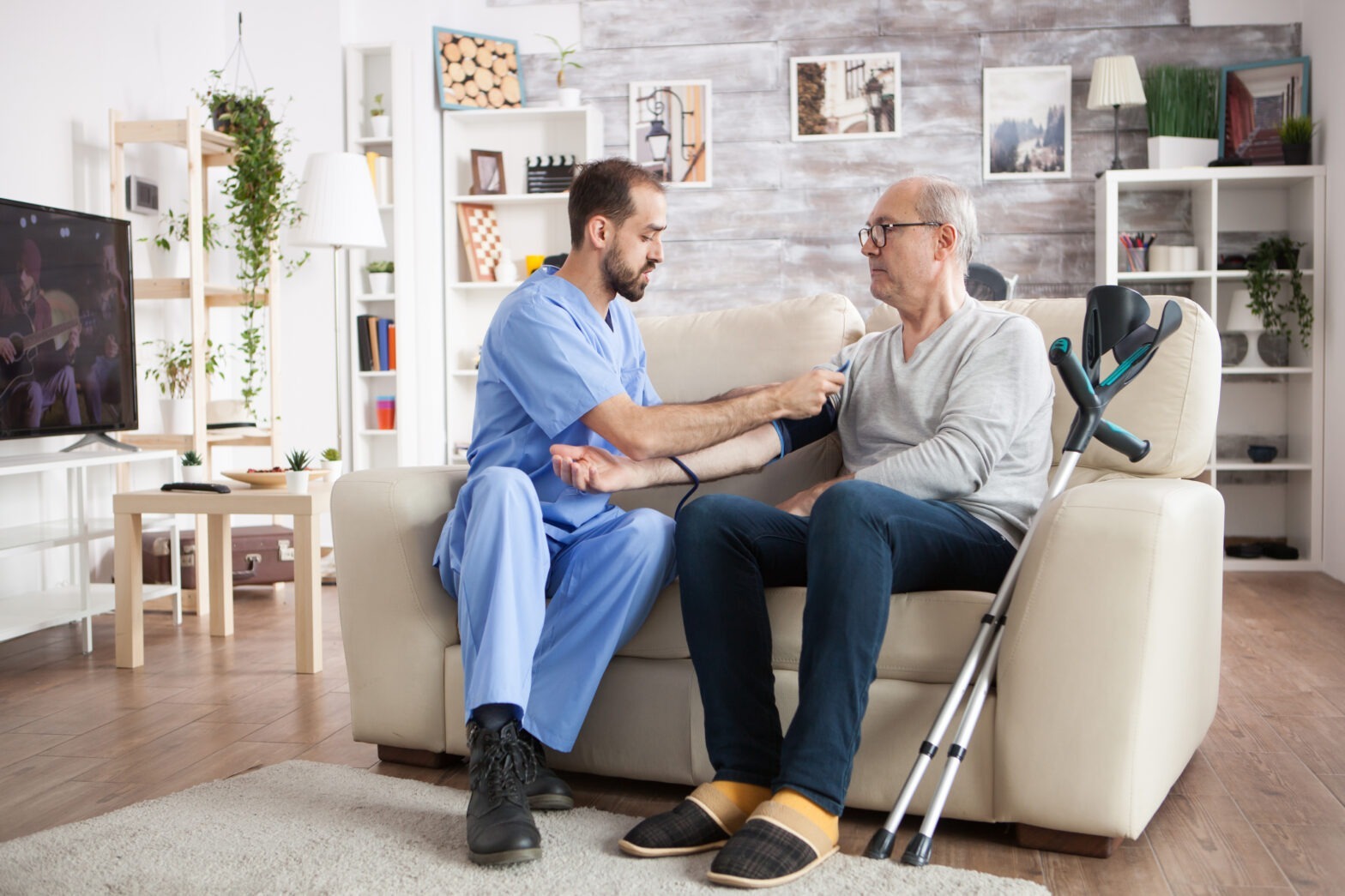home health aide assisting elderly man with blood pressure monitoring
