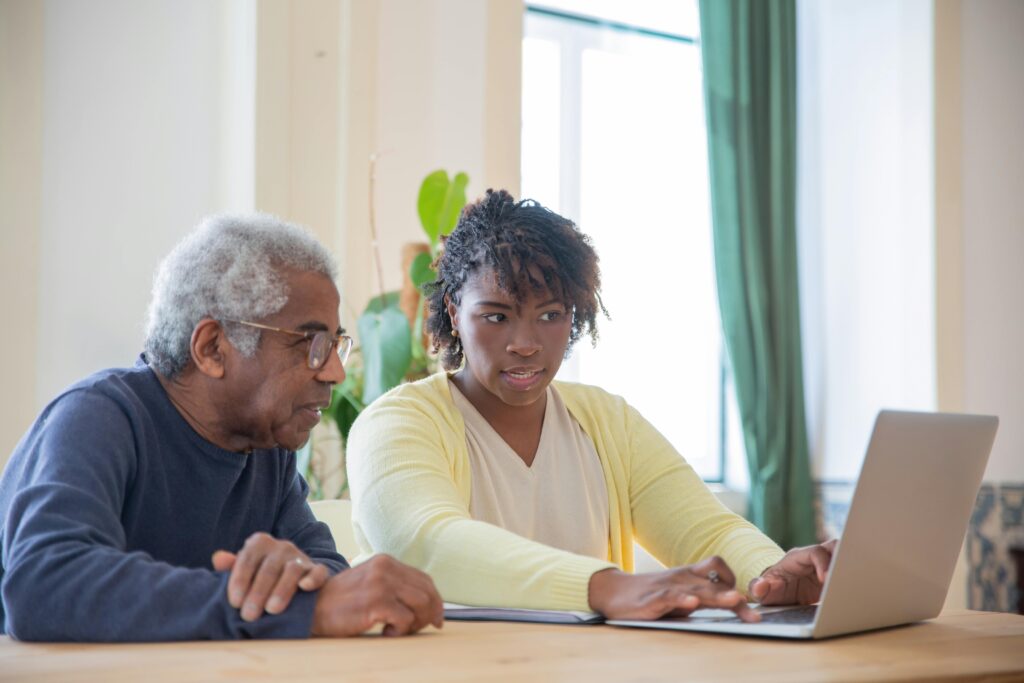 woman providing dementia care to elderly man looking at laptop computer