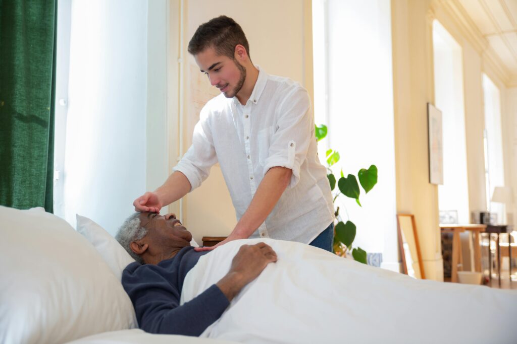 senior man in bed receiving respite care from male caregiver